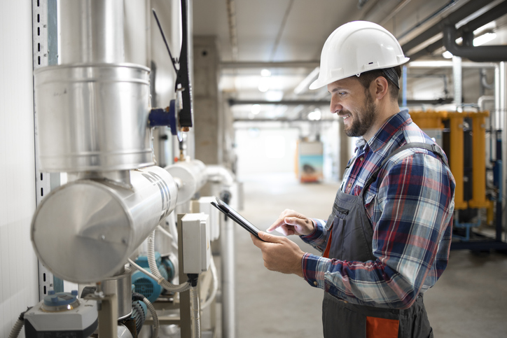 Heating Engineer Worker Holding Tablet Computer And Setting Parameters Of Heating System In Factory Boiler Room.